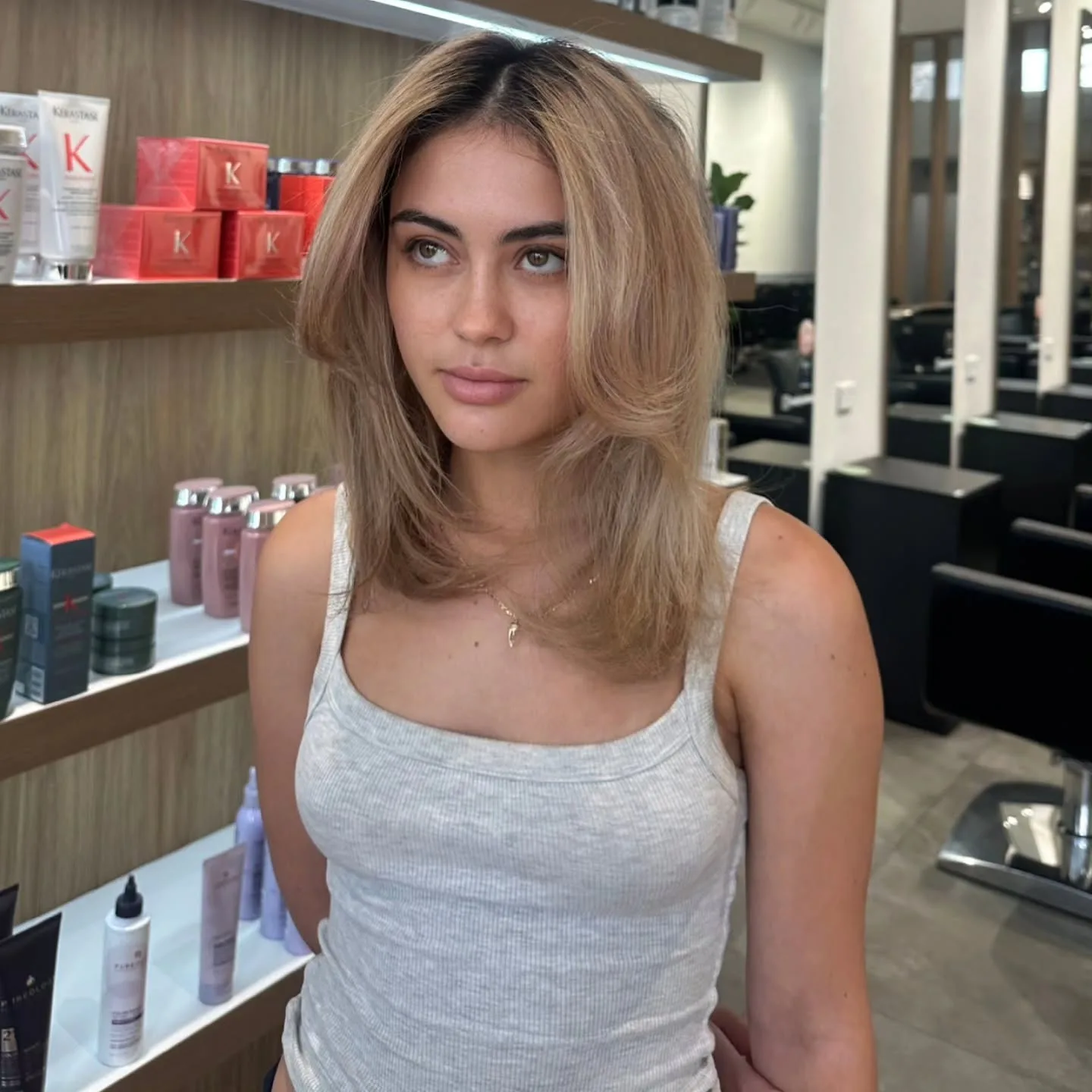 Woman with a fresh soft-blonde blow-dry at Vanity salon, Kérastase product shelves behind
