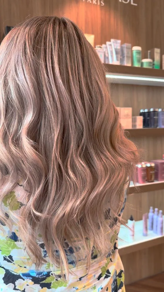Back view of long rose-gold and blonde waves against product shelves